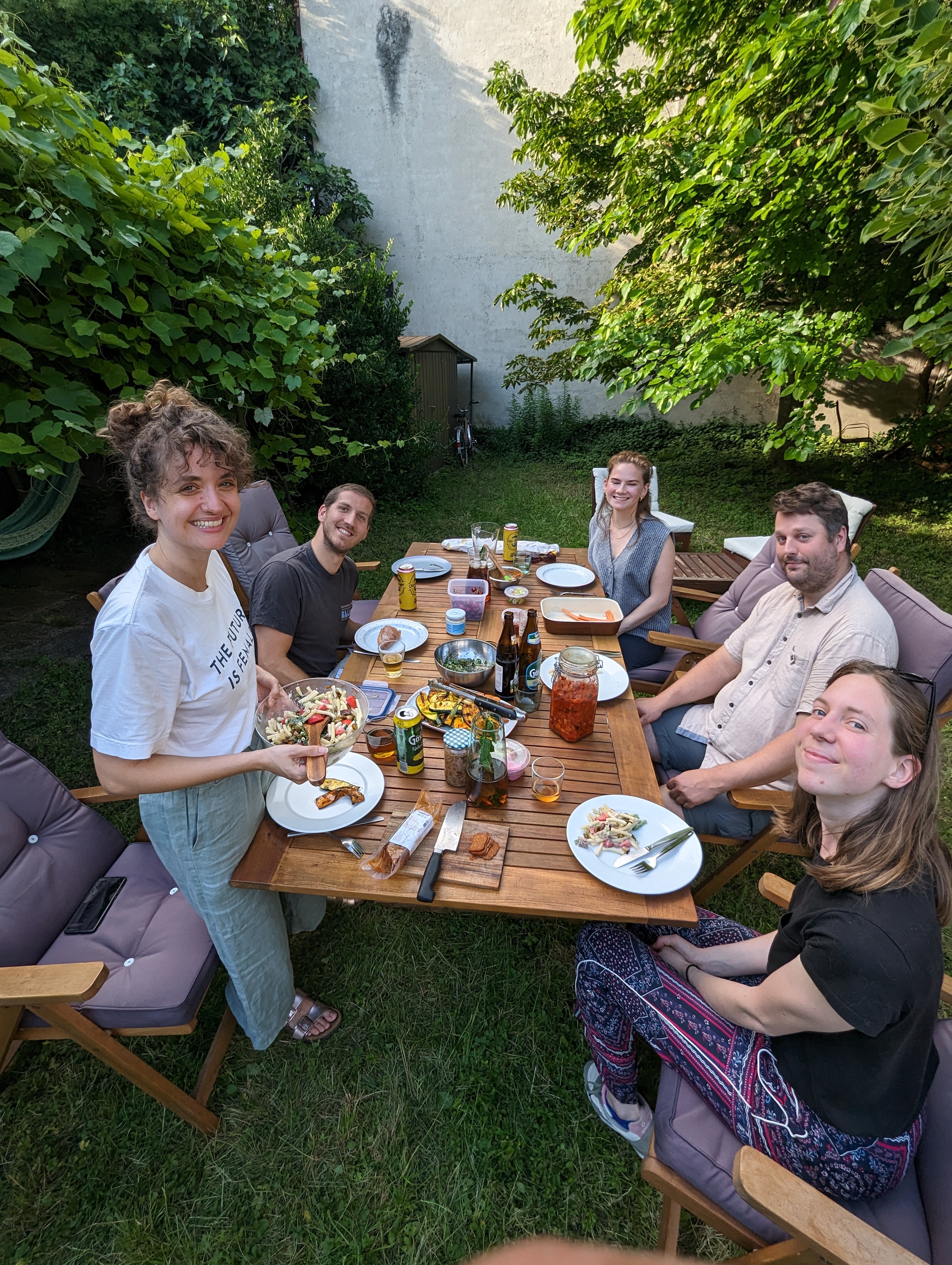 Gruppe von Freunden sitzt im Garten um einen Tisch beim gemeinsamen Essen.